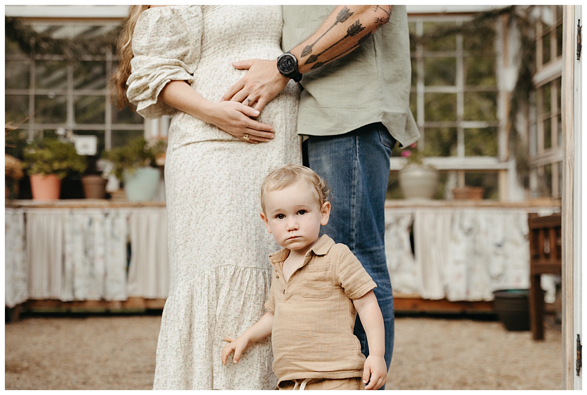dad places hand on pregnant mom's stomach while son stands in front of them by Virginia Lifestyle Photographer