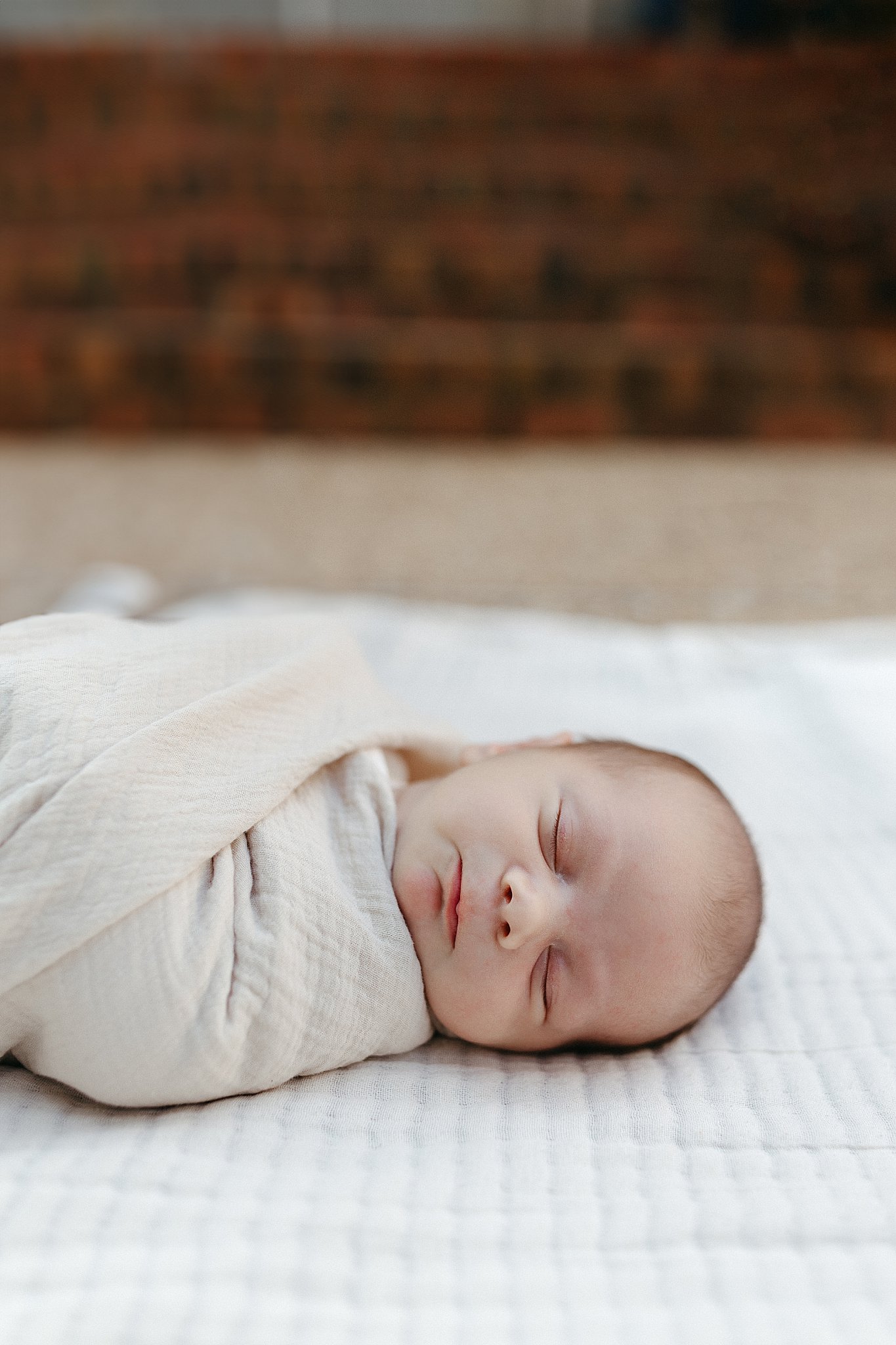 baby lays swaddled on bed in neutral in-home newborn session