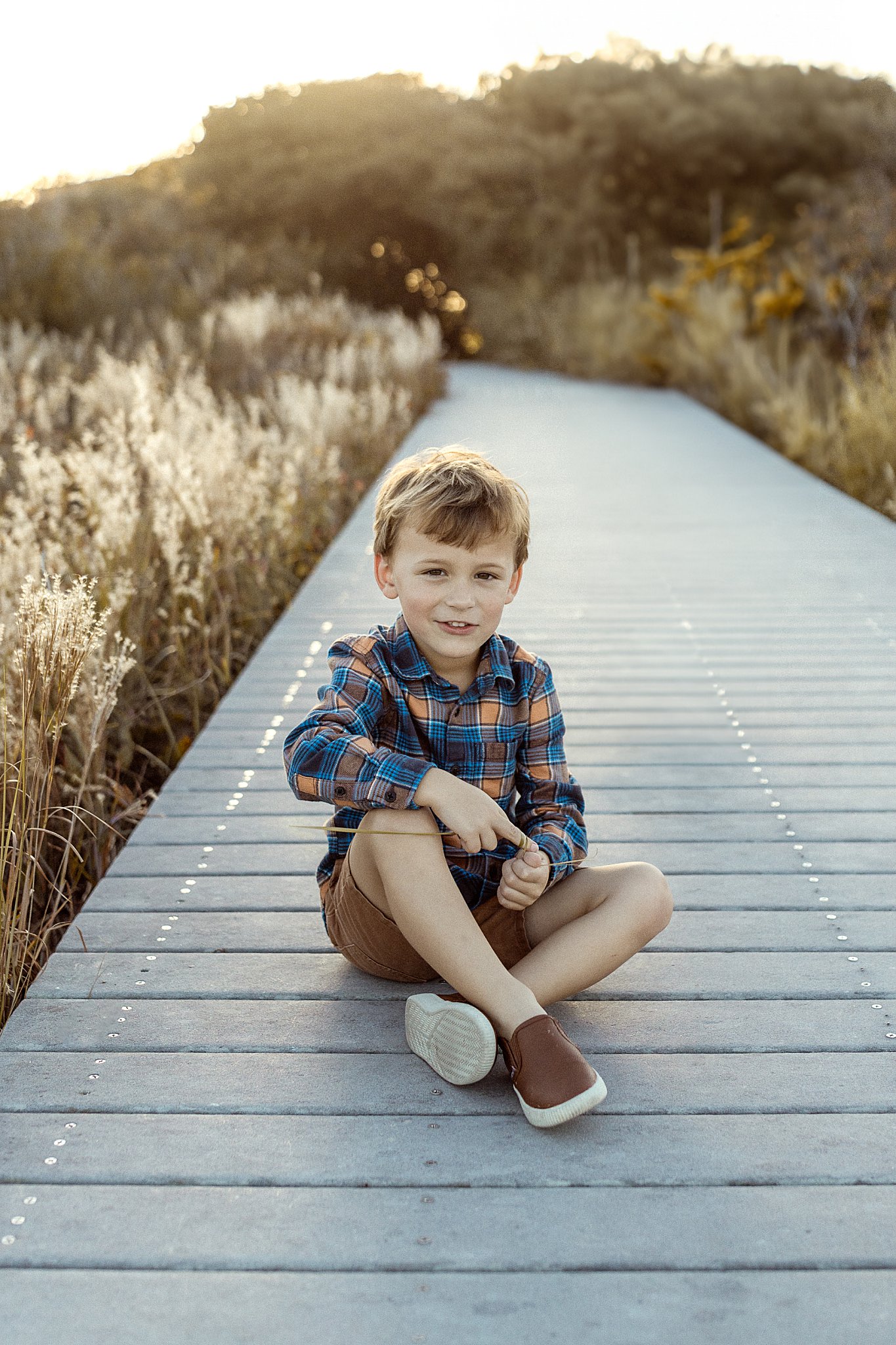 boy sits on path playing with grass by Virginia Beach photographer
