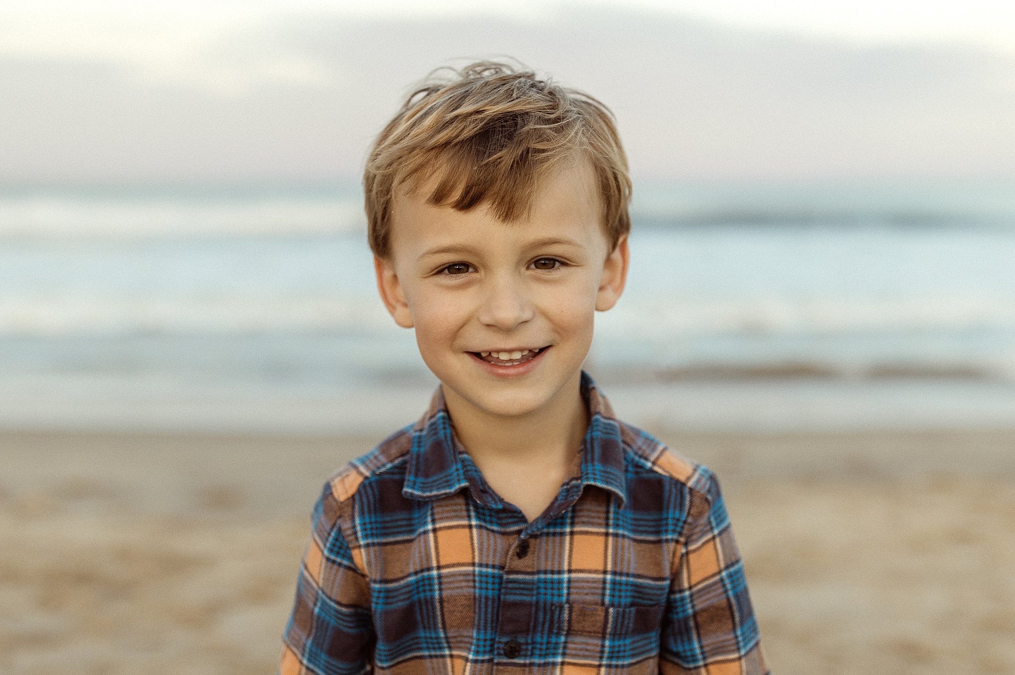 boy smiles with beach in the background at outdoor family session