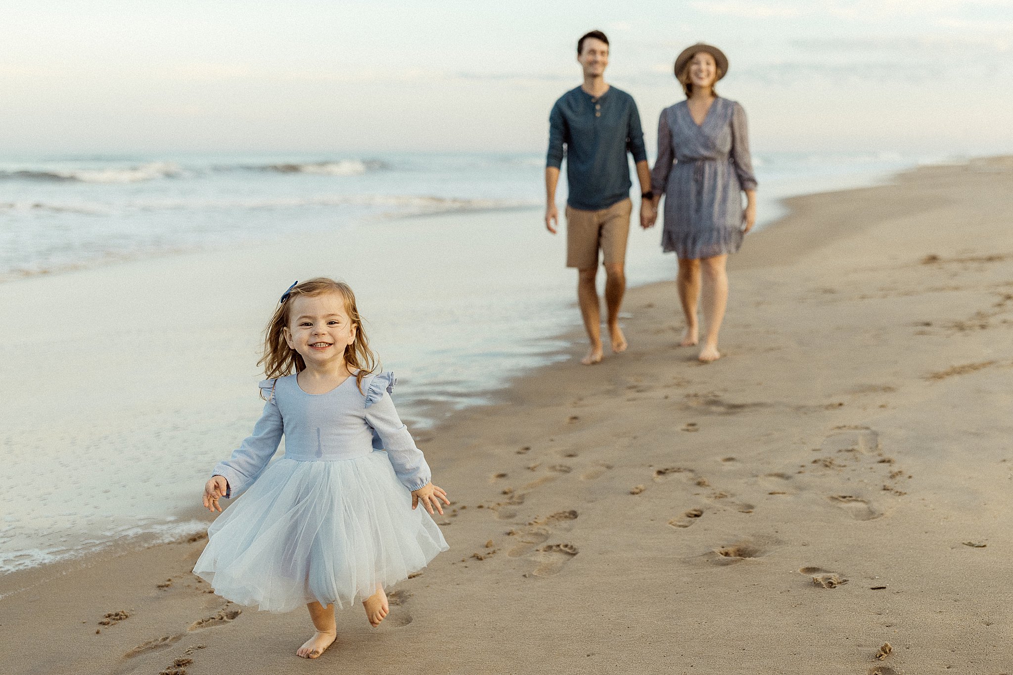 mom and dad walk behind daughter along the shore by Virginia Beach photographer