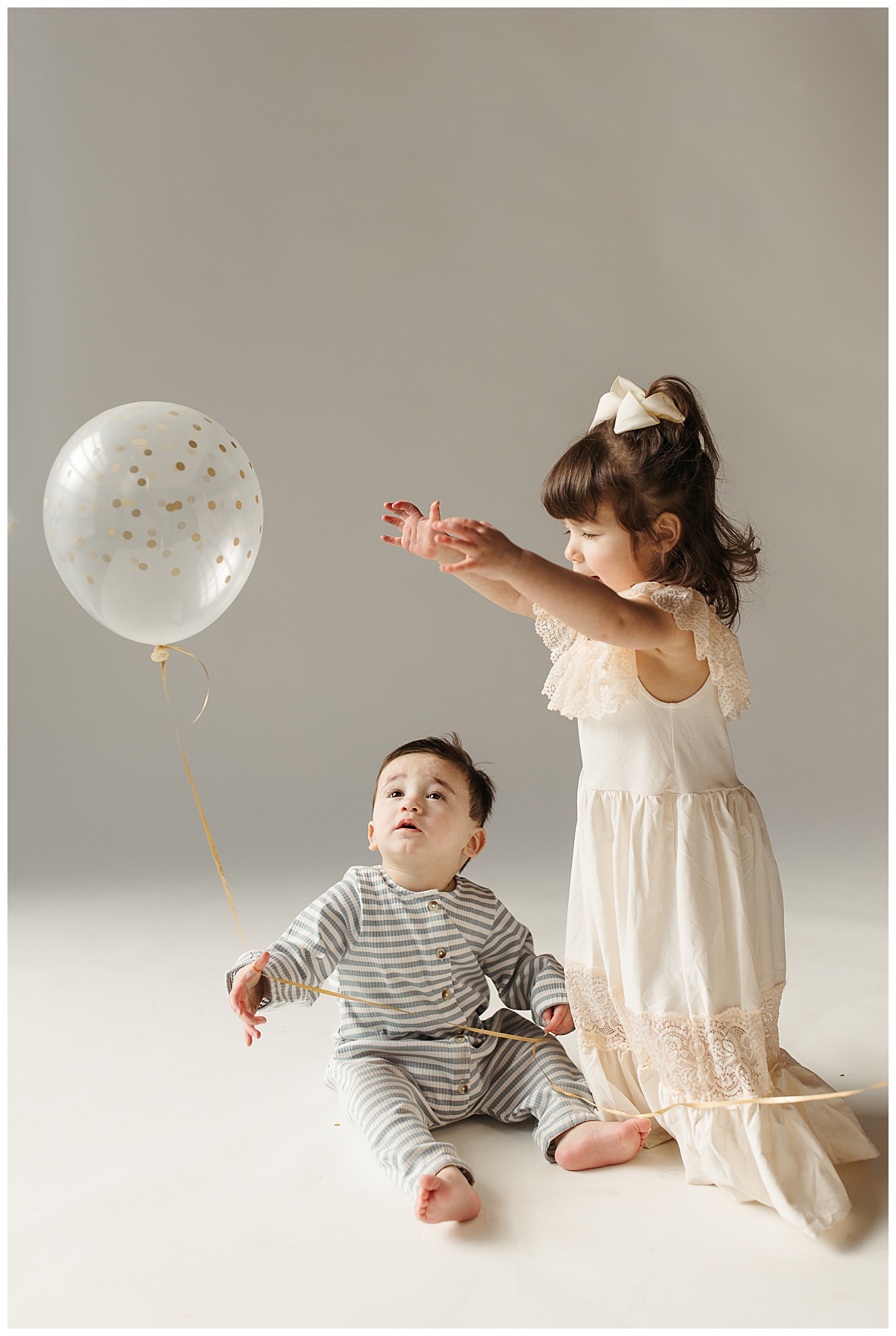 baby boy holds balloon as sister reaches for it during studio family session