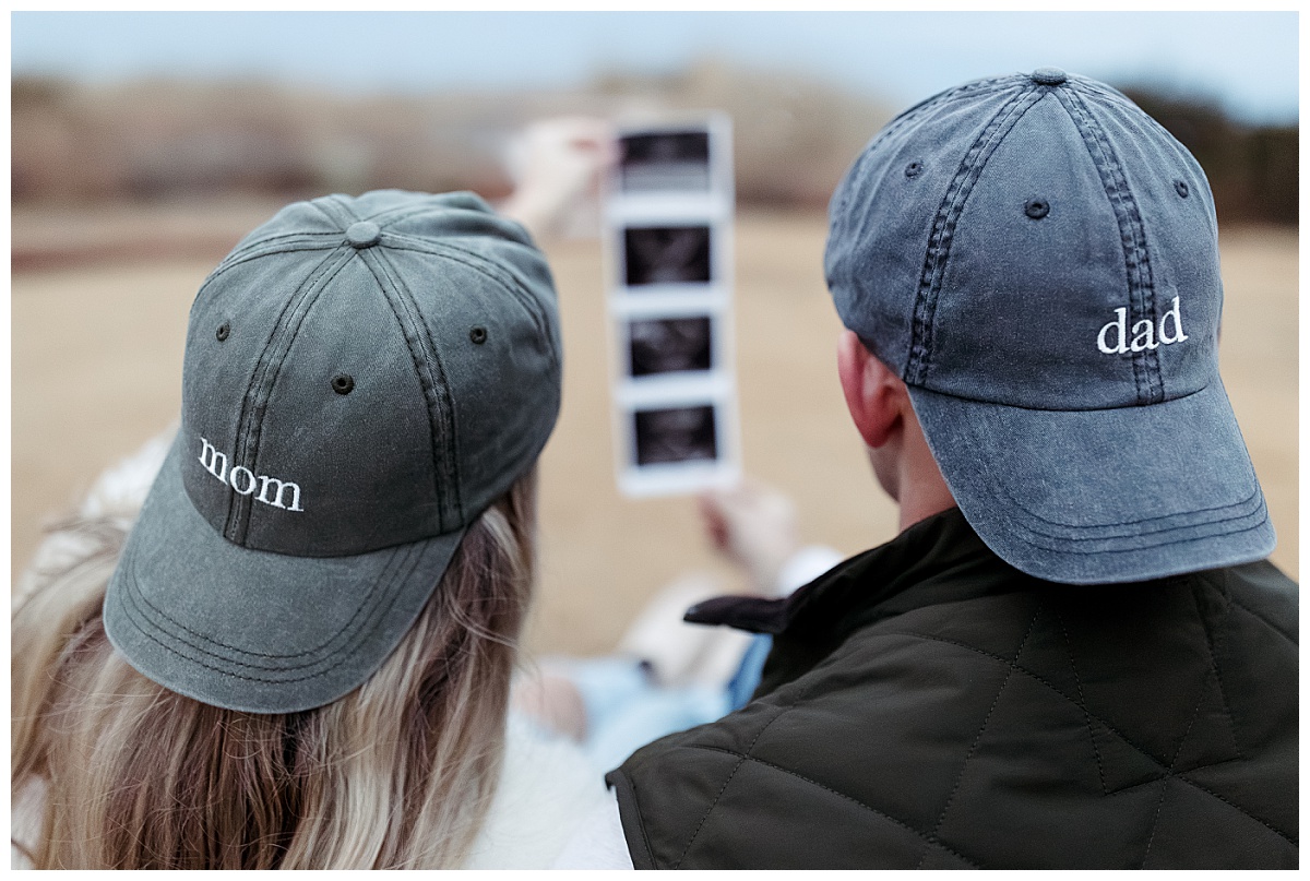 couple holds up sonogram images in mom and dad hats during pregnancy announcement session